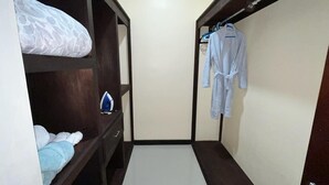 A narrow walk-through closet with wooden shelves, a hanging rack, and a white robe hanging on the right.