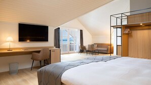 A modern hotel room with a large bed, a desk with a chair, a sofa, and a TV mounted on the wall. - Seehotel Winkelried (Stansstad)