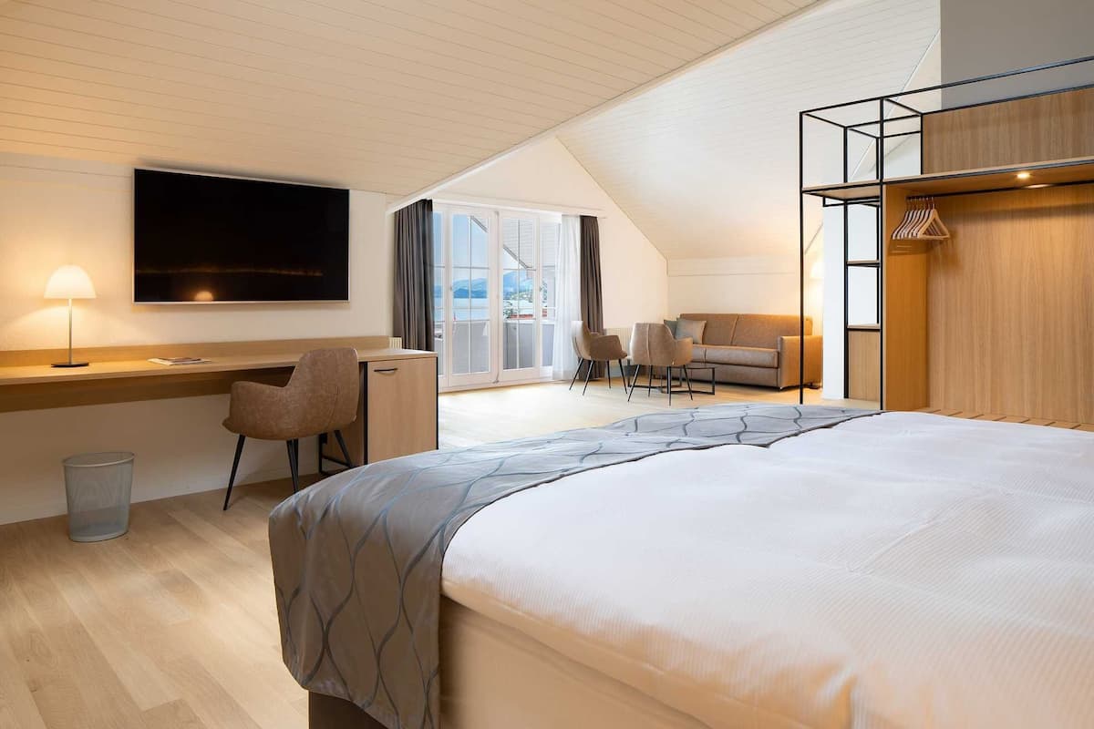 Una habitación de hotel moderna con una cama grande, un escritorio con una silla, un sofá y un televisor montado en la pared.