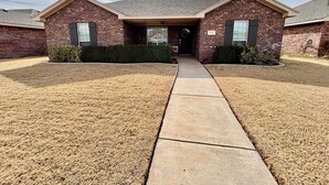 A two-story brick building with a covered entrance, a concrete pathway leading to the door, and a well-maintained lawn. - Raiderland Rest Stop - 3BR/2BA - Close to Campus (Lubbock)