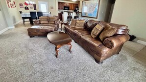 A living room with a brown leather sectional sofa, a matching ottoman, and a dining area with a table and chairs. - Raiderland Rest Stop - 3BR/2BA - Close to Campus (Lubbock)