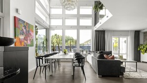 A spacious living area with a dining table, sofa, and large windows.