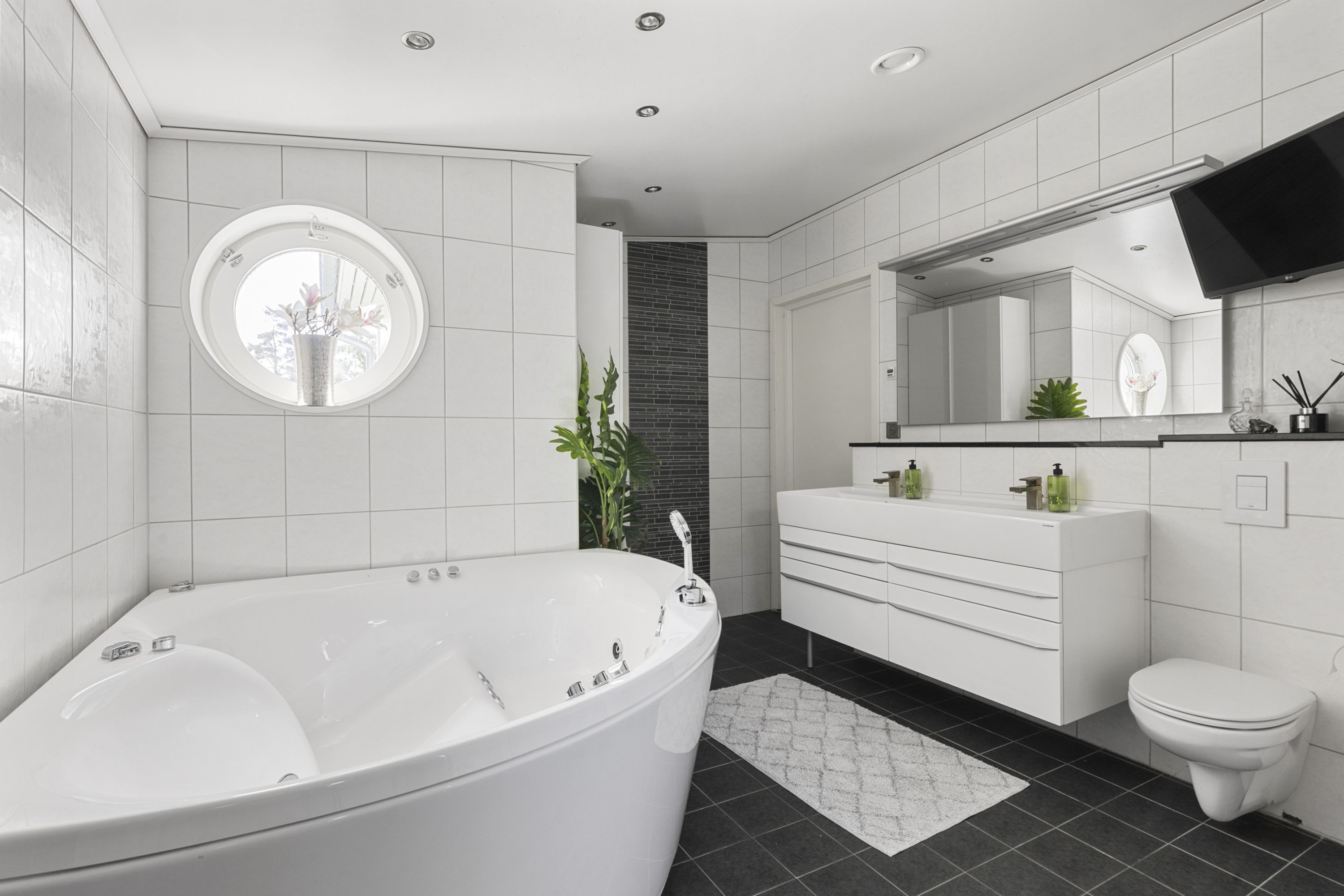 Une salle de bain moderne avec une baignoire sur pieds, un miroir rond, un meuble-lavabo blanc et des toilettes.