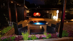 A wooden deck with a hot tub, wicker chairs, and a fire pit.