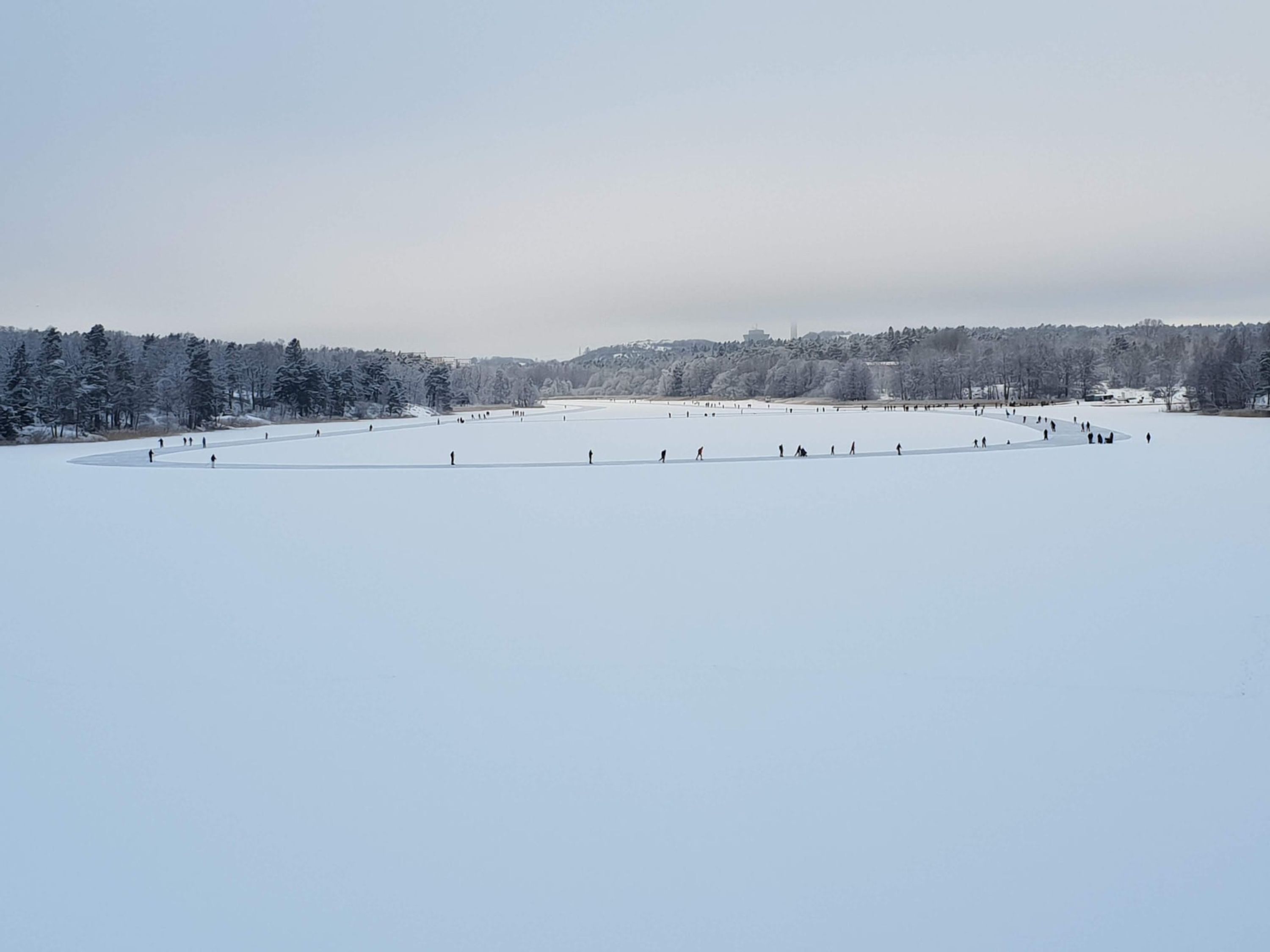 A large, open, snow-covered field with a few people scattered around.