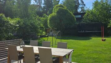 A wooden deck with a table and chairs, surrounded by a well-maintained lawn and trees.