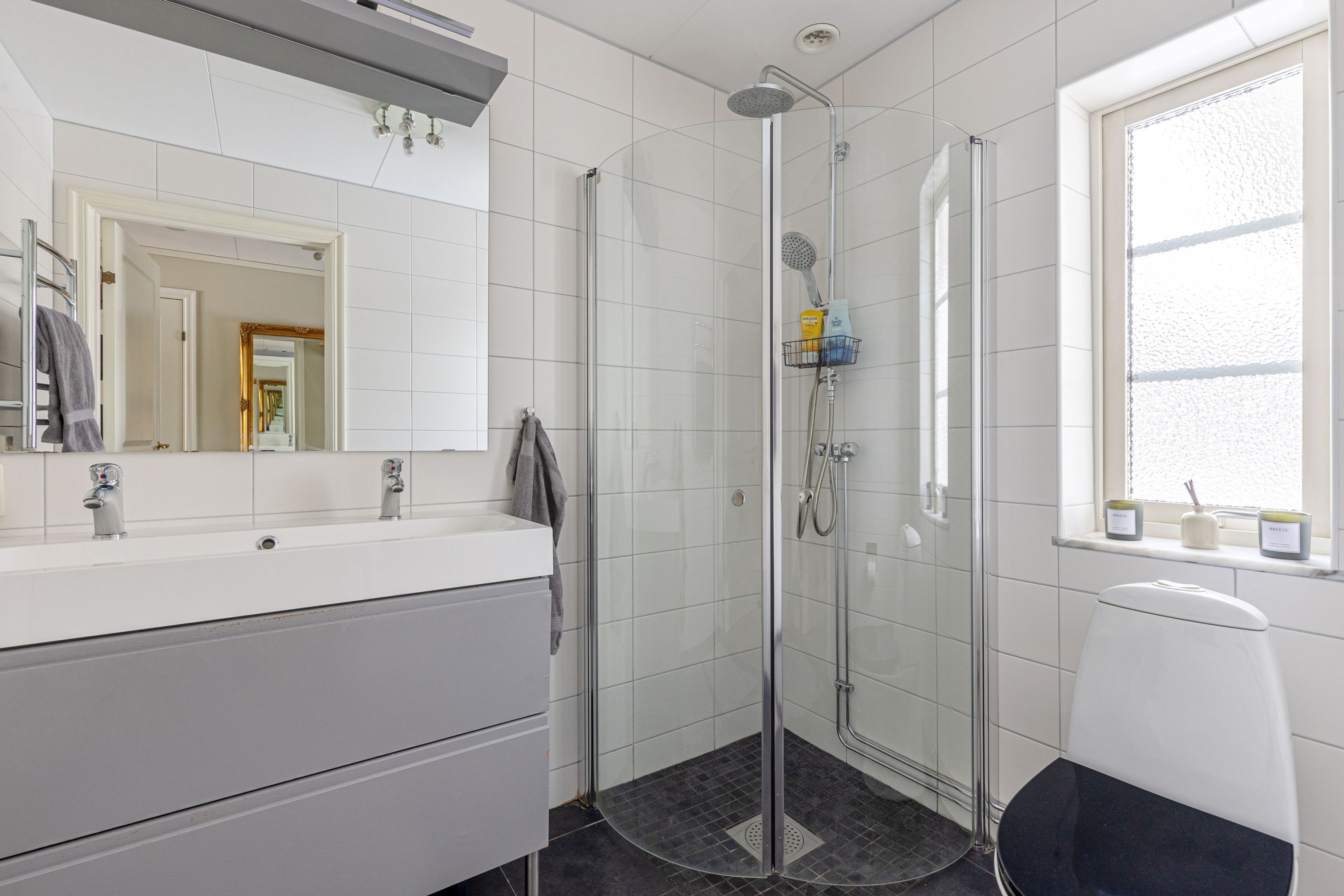 Une salle de bain moderne avec une douche à parois de verre, un lavabo blanc avec un miroir et une fenêtre donnant sur un beau paysage.