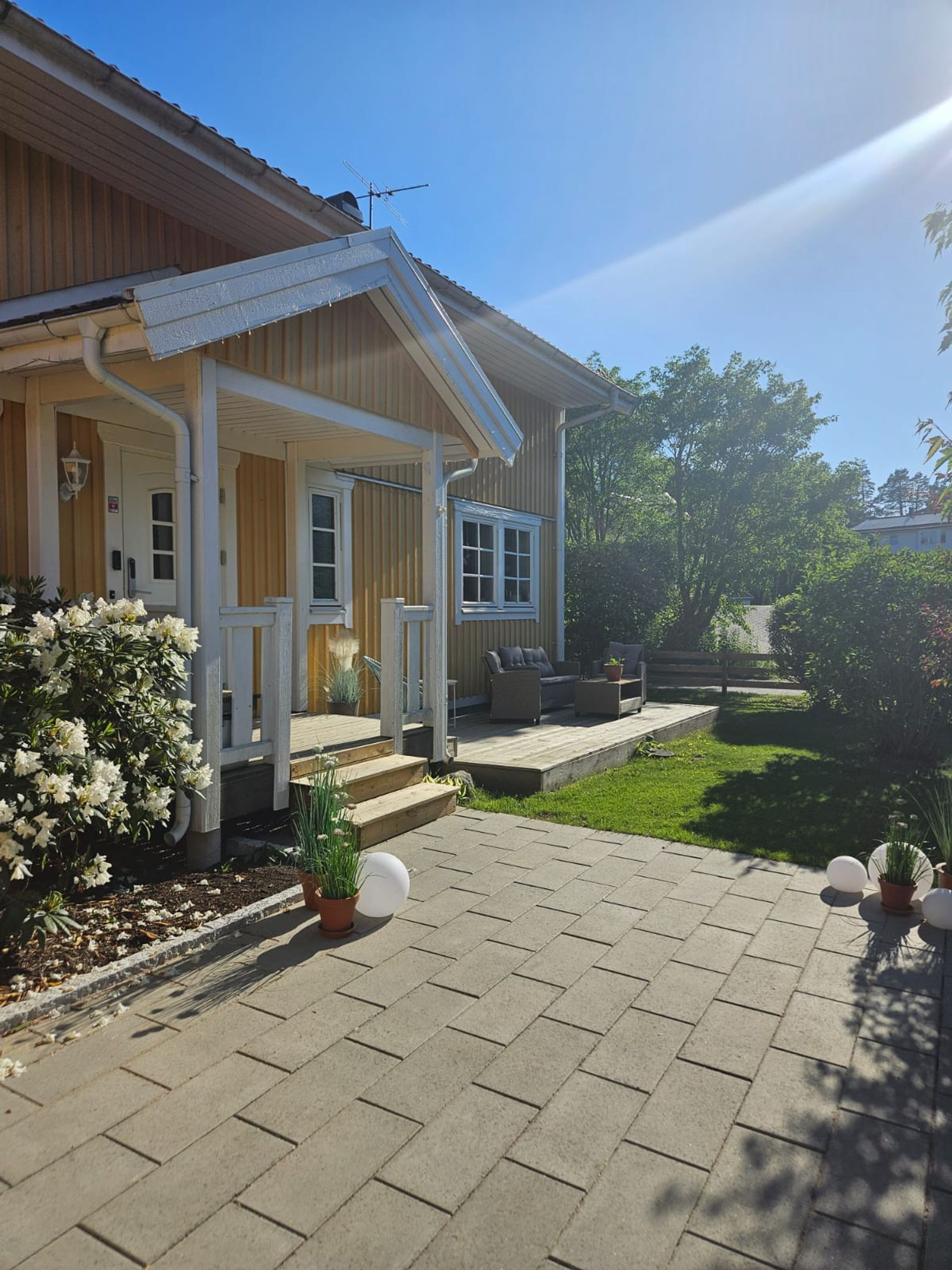 A two-story house with a covered porch, a small garden, and a paved driveway.