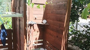 A wooden outdoor shower structure with a stone pathway leading to it, surrounded by greenery.