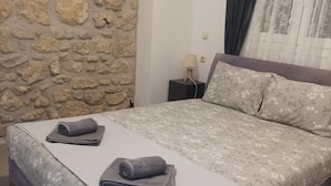 A bedroom with a stone wall, a bed with floral bedding, and a nightstand with a lamp.