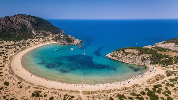 An aerial view of a coastal area with a sandy beach, clear blue waters, and boats.