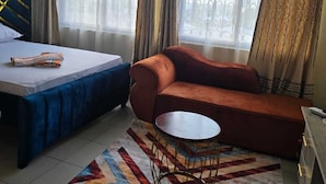 Een kamer met een bed, een slaapbank, een klein rond tafeltje en een kamerbreed tapijt met dessin.
