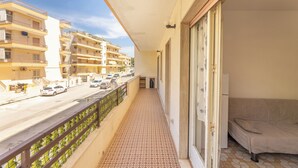 Ein Balkon mit einem gemusterten Boden, einer Couch und Blick auf eine Straße mit parkenden Autos und Gebäuden.