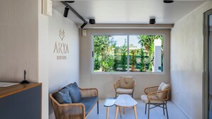A hotel room with a reception desk, a sofa, two chairs, a small table, and a large window with a view of greenery. - Arya Hotel (Kassandra)