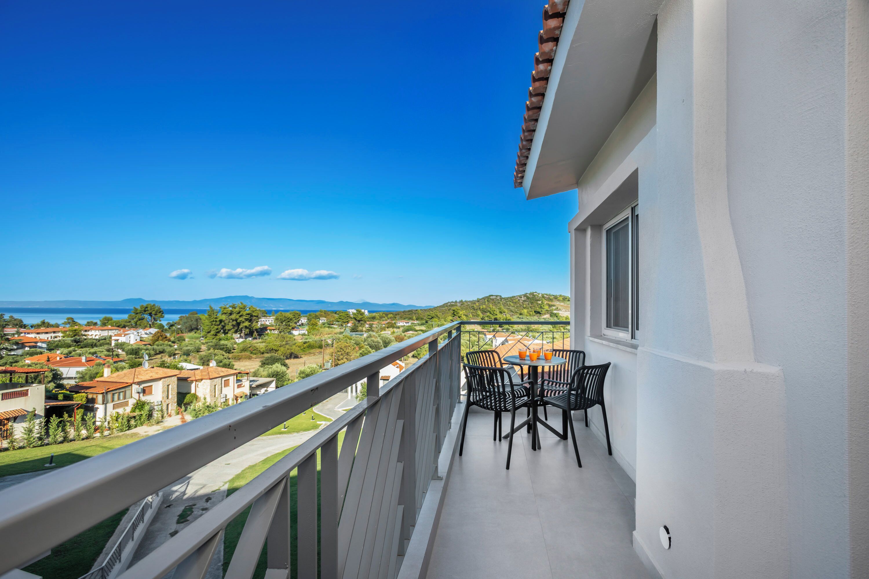 A balcony with a table and chairs, overlooking a residential area and a body of water.