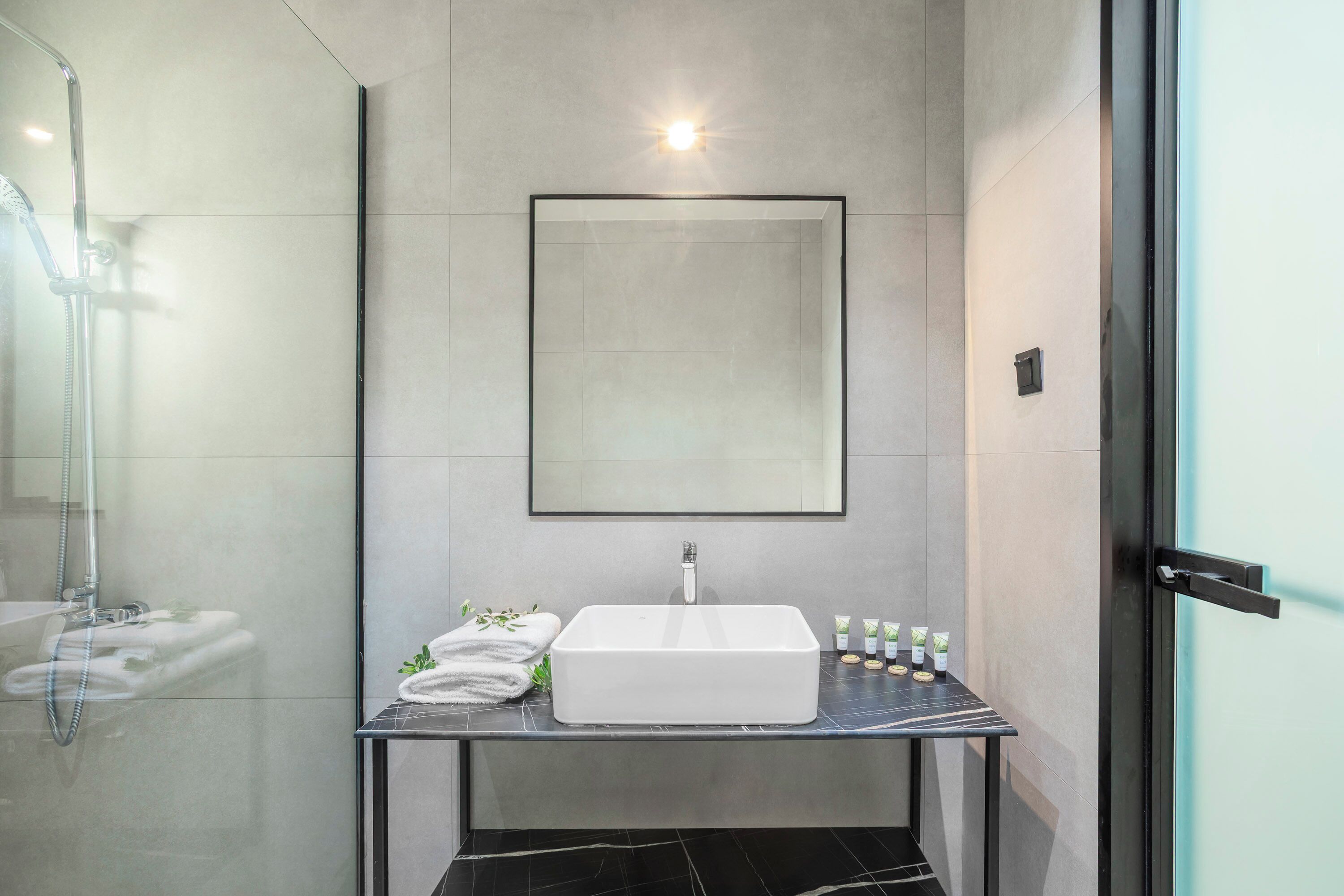 A modern bathroom with a white sink, a glass shower enclosure, and a framed mirror above the sink.