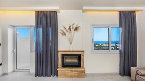 A living room with a fireplace, a sofa, a coffee table, and a view of the sea. - Arya Hotel (Kassandra)
