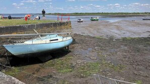 Un bote atracado en una orilla embarrada con una zona cubierta de hierba y algunas personas al fondo.