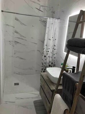 Un baño moderno con cabina de ducha de vidrio, un lavabo blanco y un mueble de tocador de madera.