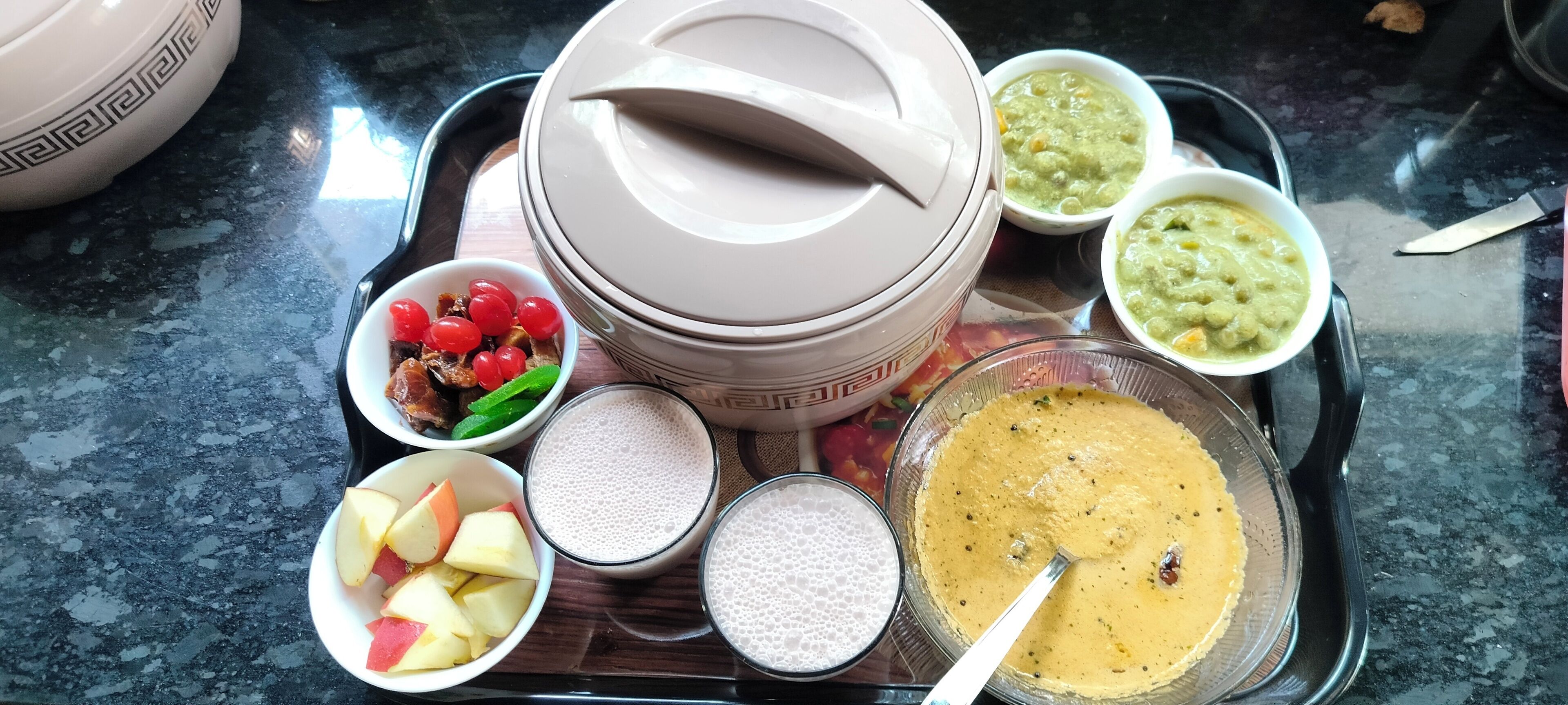 A tray with various food items including bowls of fruit, a bowl of soup, and a bowl of porridge.