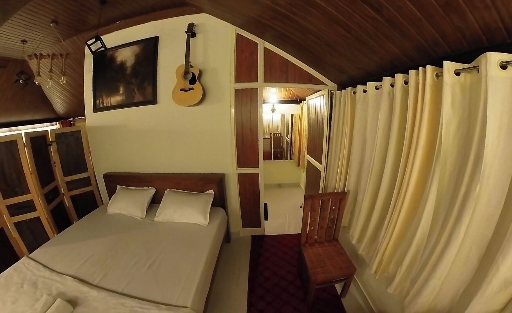 A bedroom with a bed, a guitar, a chair, and a mirror.