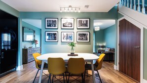 Un coin repas avec une table blanche et des chaises jaunes, des tableaux encadrés au mur et un plancher en bois.