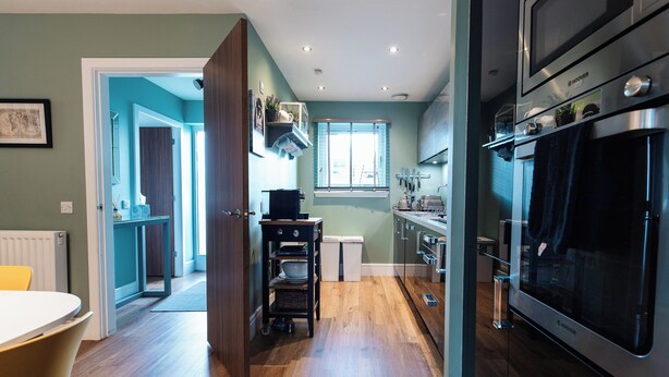 Une cuisine moderne avec un plancher en bois, des appareils électroménagers intégrés et une fenêtre.