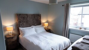 Un lit bien fait, avec du linge de lit blanc, deux lampes de chevet, une tête de lit en bois et une fenêtre avec des rideaux.