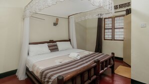 A neatly made bed with a striped bedspread, a white canopy, and a wooden headboard. - Dream Jet Suites (Entebbe)