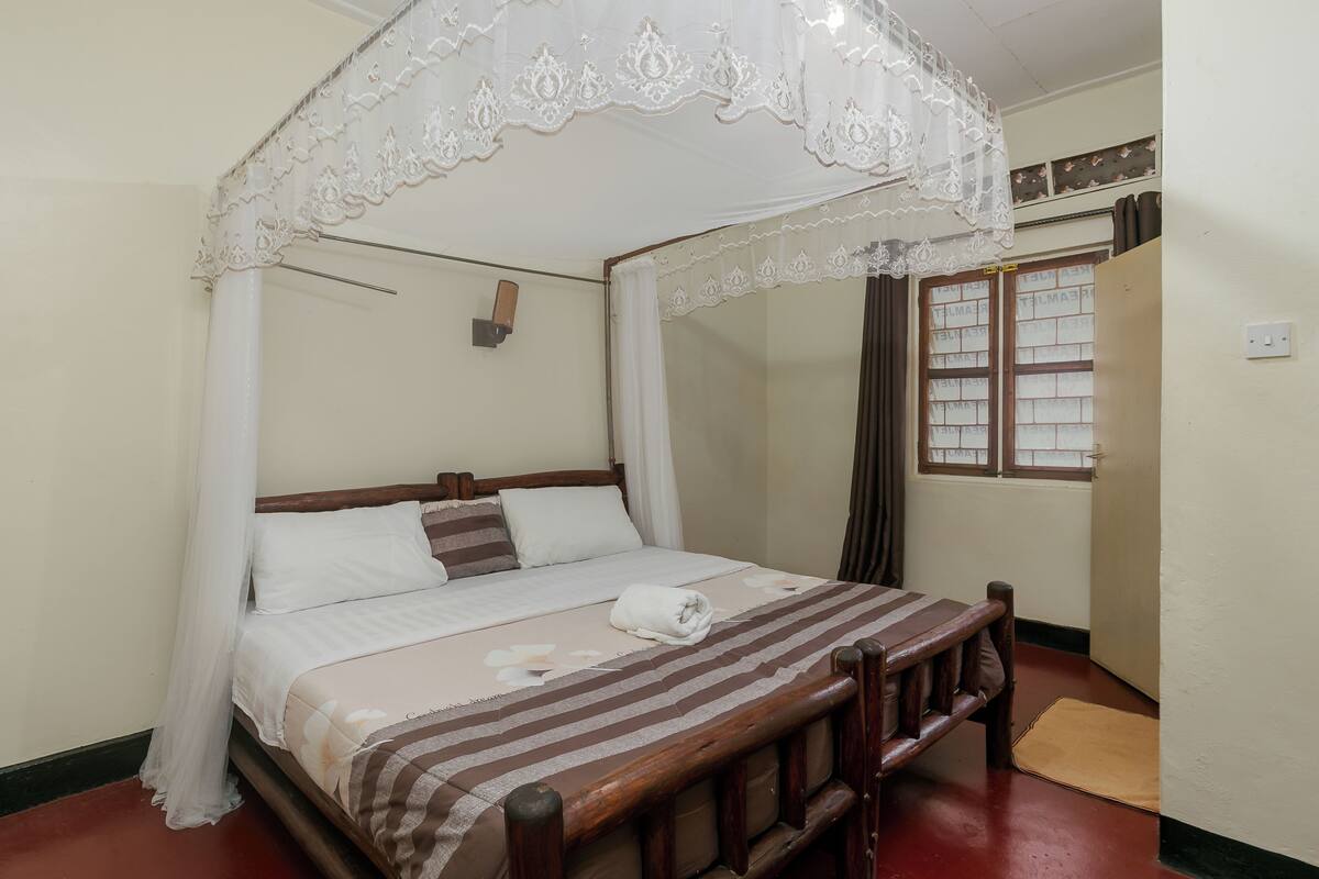 A neatly made bed with a striped bedspread, a white canopy, and a wooden headboard.
