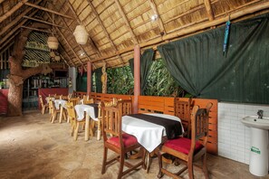 An indoor dining area with wooden tables and chairs, a thatched roof, and a bar area with bottles. - Dream Jet Suites (Entebbe)