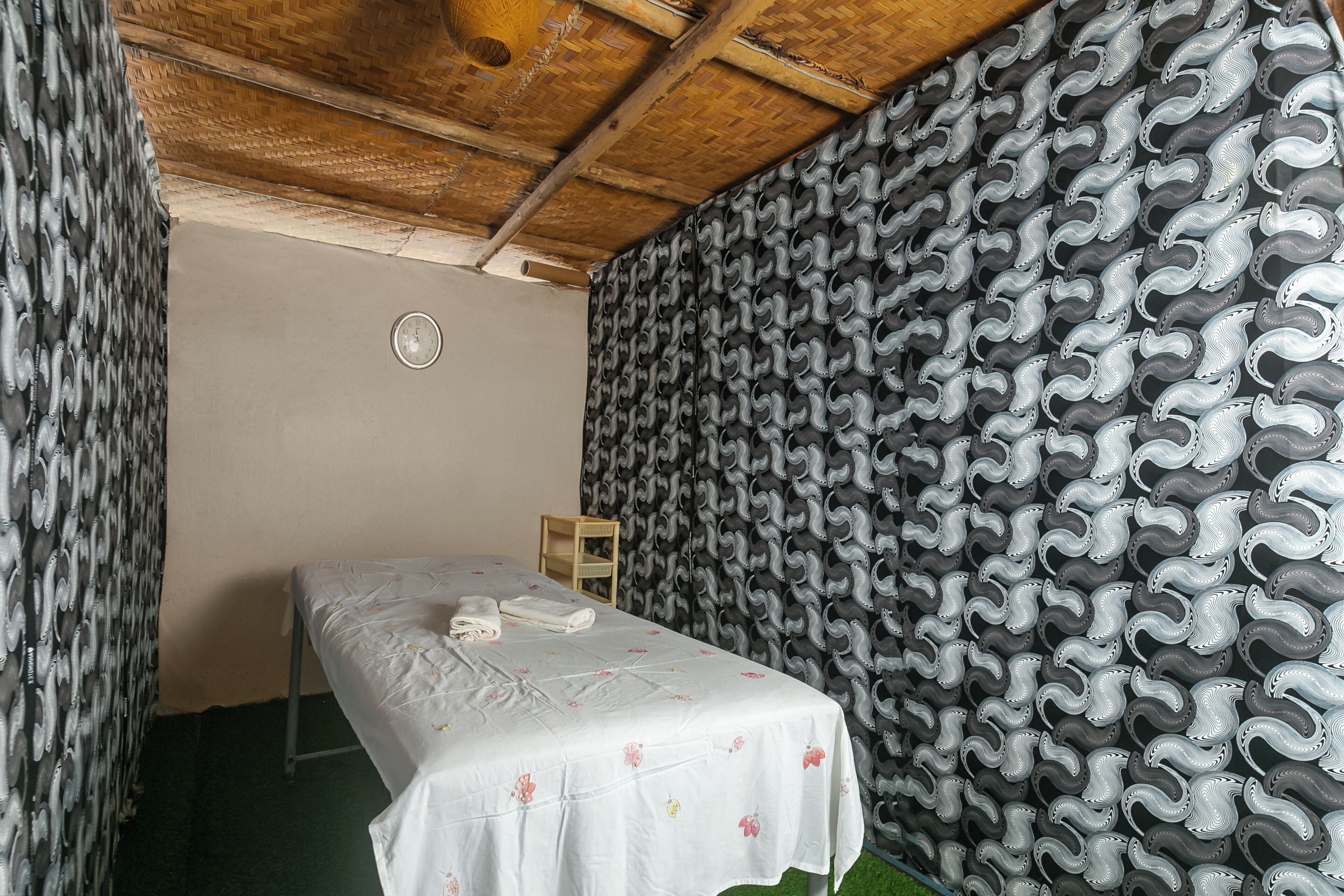 A room with a bed, a wall clock, and a patterned wallpaper.