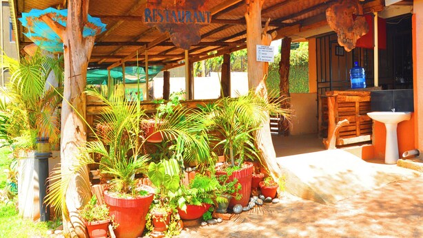 A rustic outdoor seating area with a wooden roof, surrounded by potted plants and a sign indicating a restaurant. - Dream Jet Suites (Entebbe)