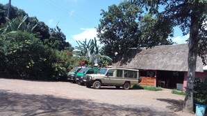 A row of vehicles parked in front of a building with a thatched roof, surrounded by greenery. - Dream Jet Suites (Entebbe)