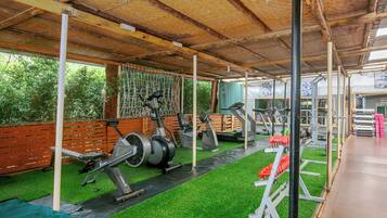A covered gym with exercise equipment, artificial grass, and a wooden deck.