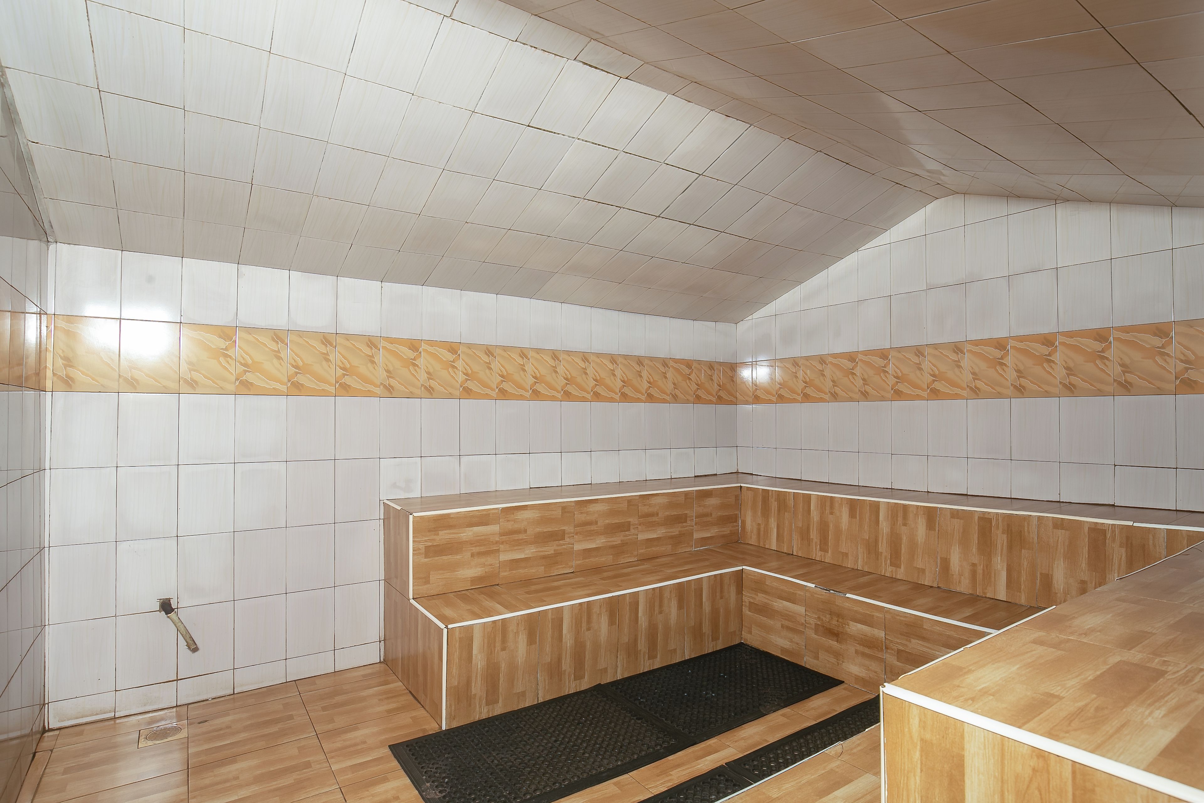 A room with a tiled ceiling, a wooden bench, and a black mat on the floor.