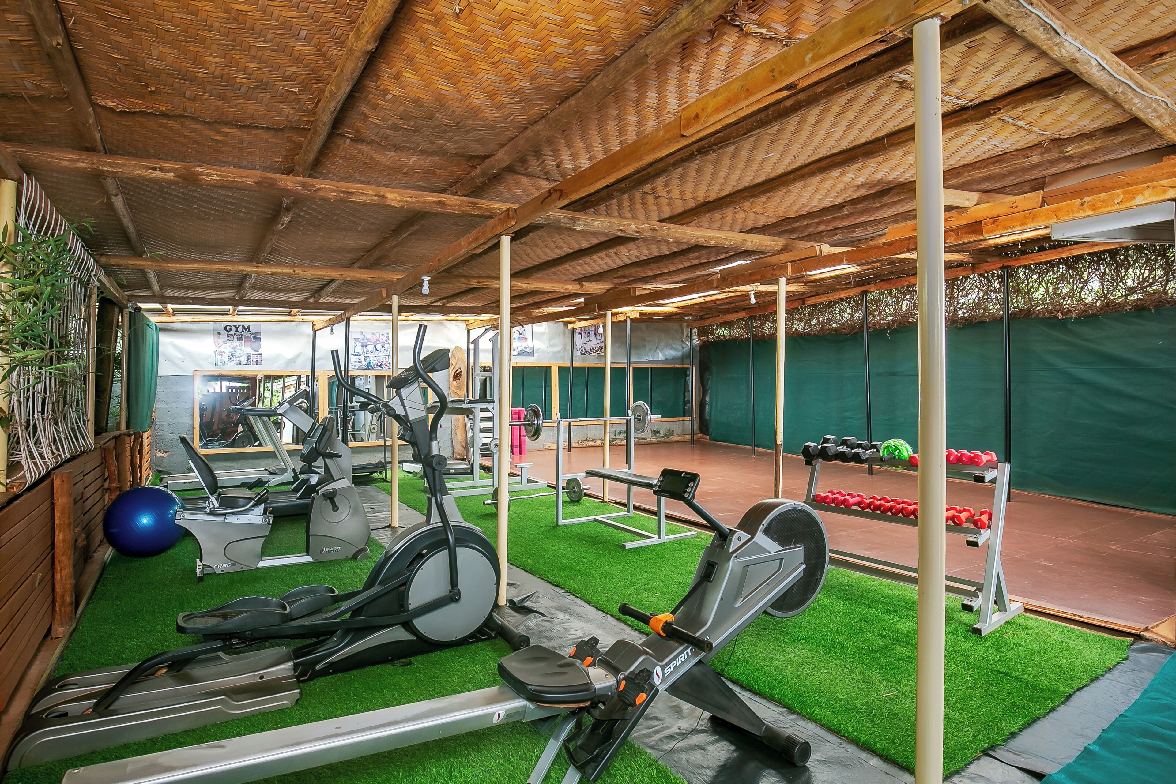 Un gimnasio con equipamiento de ejercicio, césped artificial verde y una zona cubierta con techo de madera.