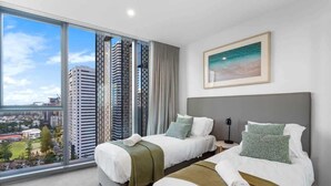 A hotel room with two beds, a large window with a city view, and a framed picture on the wall.