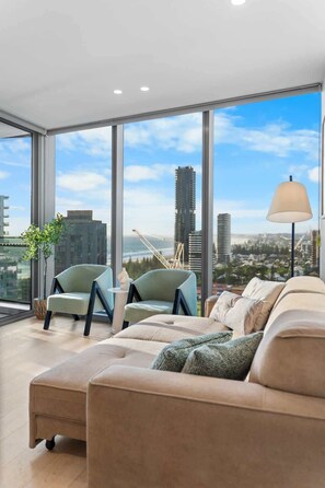 A modern living room with a large window, a sofa, two armchairs, and a floor lamp. - Beachfront Luxe | New Stay w/ Infinity Pool + Gym (Broadbeach)