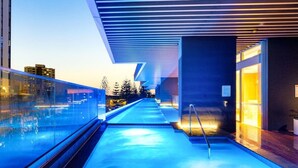 A modern building with a glass facade, a pool area, and a view of the cityscape.