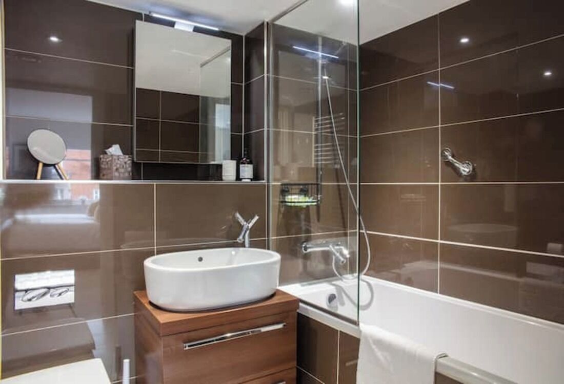 Ein modernes Badezimmer mit einer großen Badewanne, einem runden Spiegel und einem hölzernen Waschtisch.