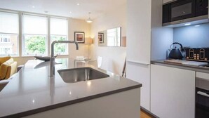 A modern kitchen with a central island, stainless steel sink, and a microwave. - Kensington High Street One Bed Flat (London)