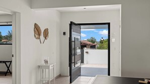 A modern interior with a white wall, a glass door leading to an outdoor area, and a small white table with a glass.