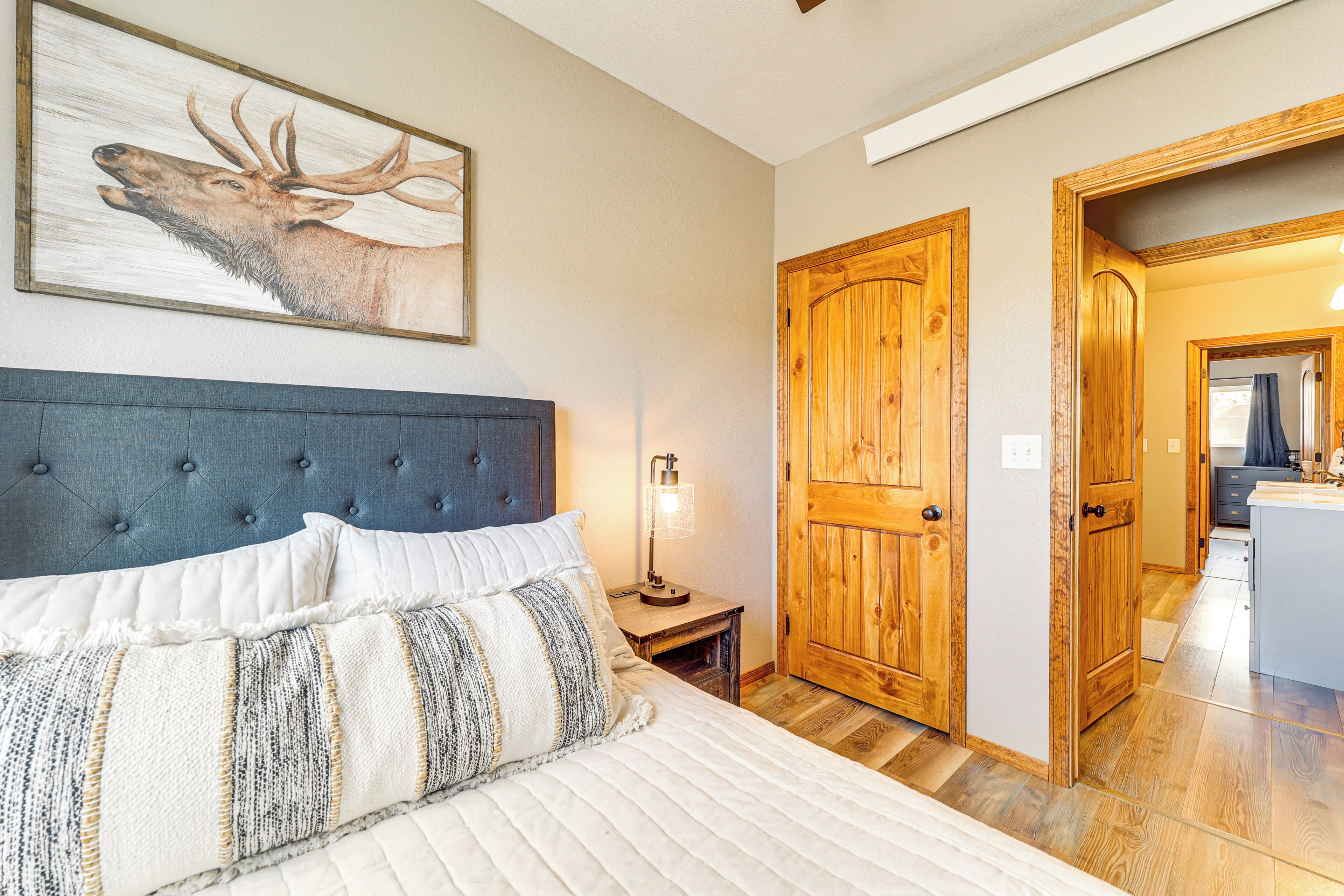 A bedroom with a bed, a nightstand, a lamp, a wooden door, and a painting of a deer.