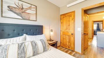 A bedroom with a bed, a nightstand, a lamp, a wooden door, and a painting of a deer.