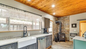 Una cocina con encimeras de granito, lavavajillas, pared de piedra y estufa de leña.