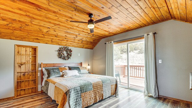 Un dormitorio con techo de madera, una cama con colcha, un armario de madera y un ventanal con cortinas.