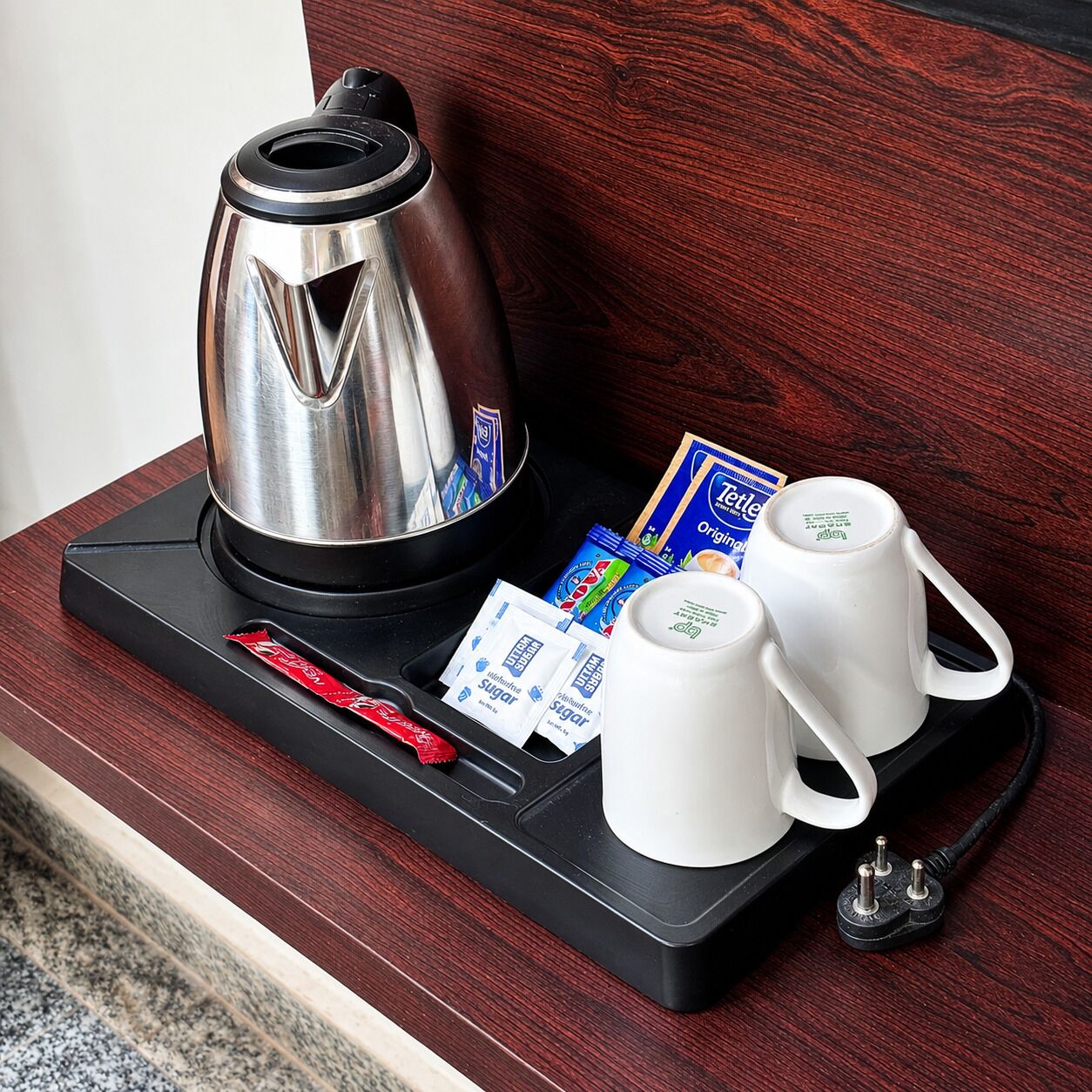 A coffee maker, sugar packets, and two white cups on a tray.