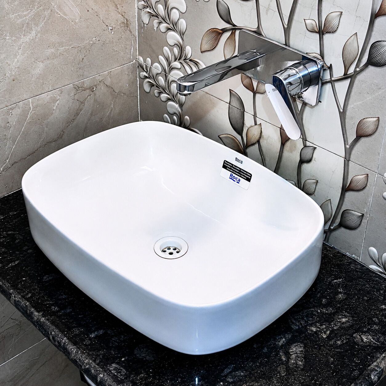 A white sink with a modern faucet, set against a wall with a leaf-patterned tile design.