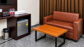 A hotel room with a TV, a desk with a trash can, a brown leather chair, a wooden table, and a curtain. - The Manthan Stays (Vrindavan)